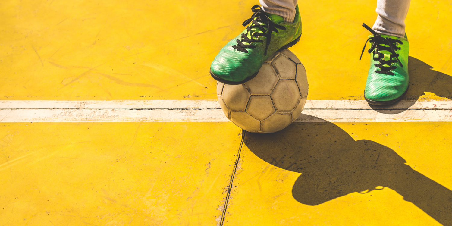 Eine Person hält mit dem linken Fuß einen Fußball fest und steht dabei auf einer Linie