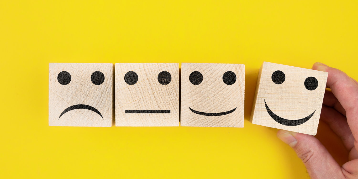 4 Holzsteine, auf denen ein trauriges, ein neutrales, ein fröhliches und ein sehr fröhliches Smiley abgebildet ist