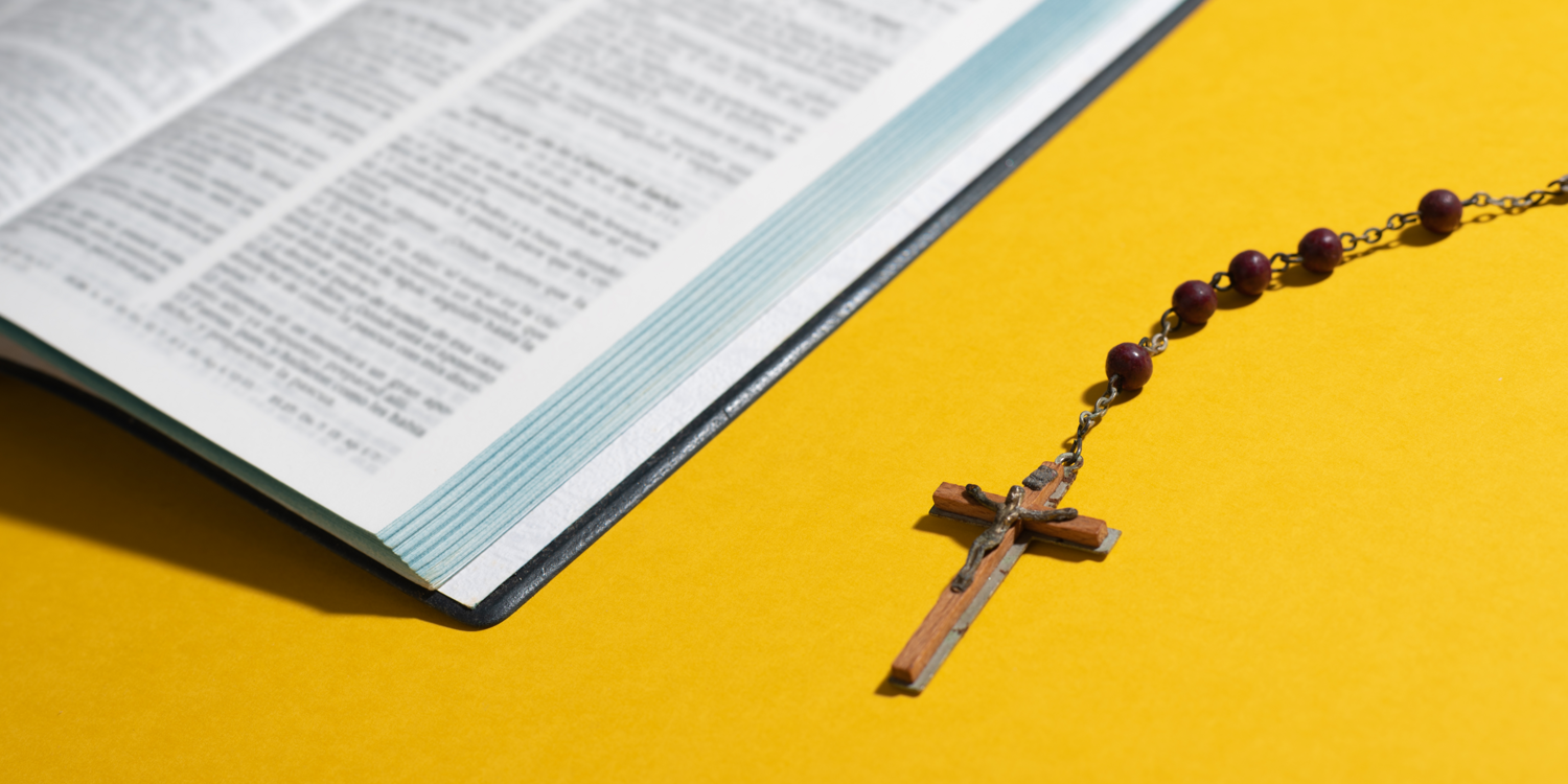 canva neben einer Bibel liegt ein Rosenkranz von dem man das Kreuz und fünf Perlen sieht