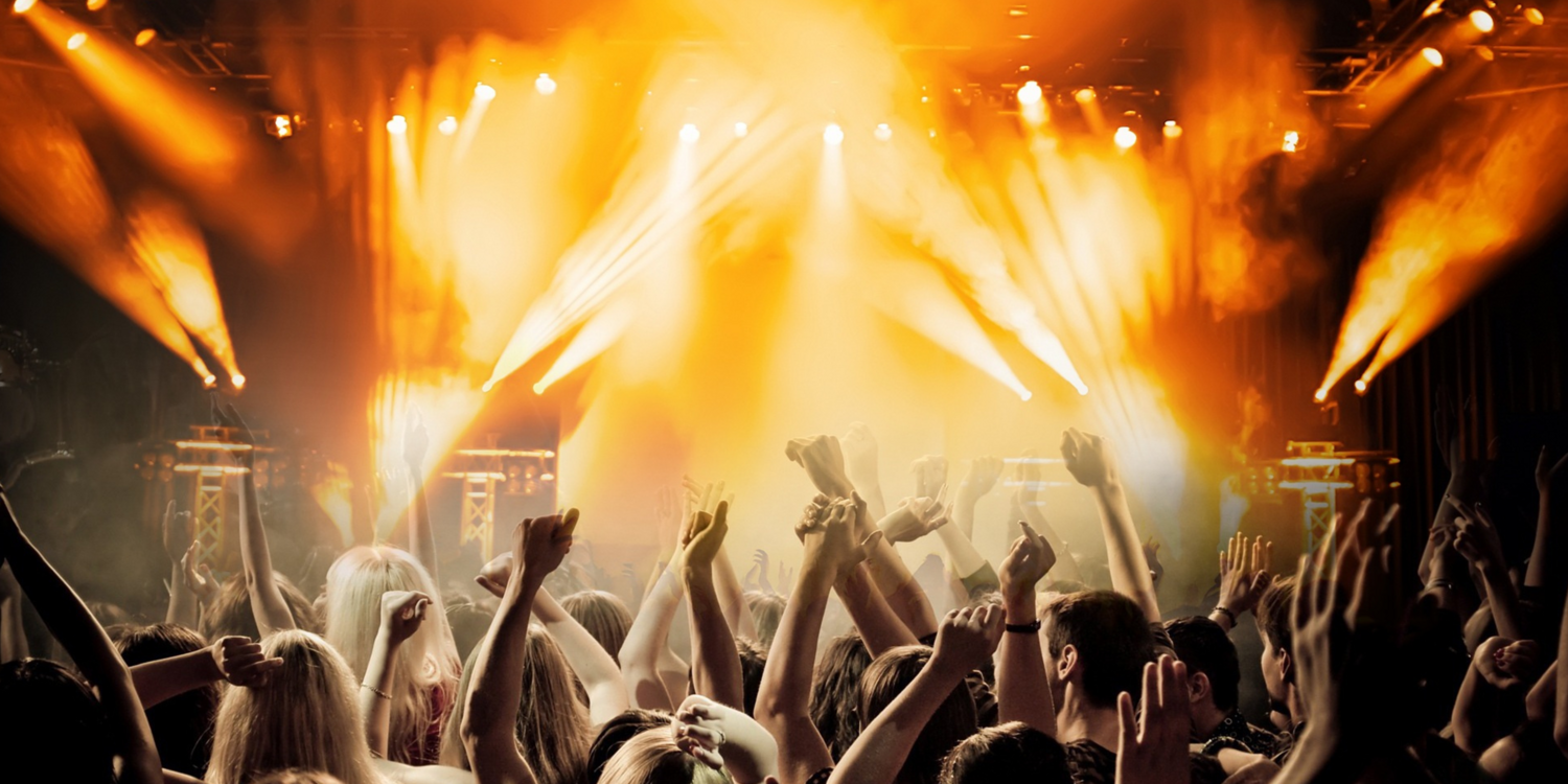 Personen halten ihre Hände auf einem Konzert in die Höhe | im Hintergrund sieht man die Bühne